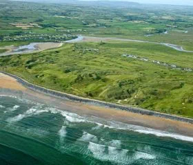 Waves crashing onto beach with Lahinch golf club nearby,