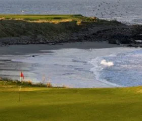 The beach with waves crashing on the shore and view of the hole on the golf course at the Crail Balcomie Links at St Andrews in Scotland