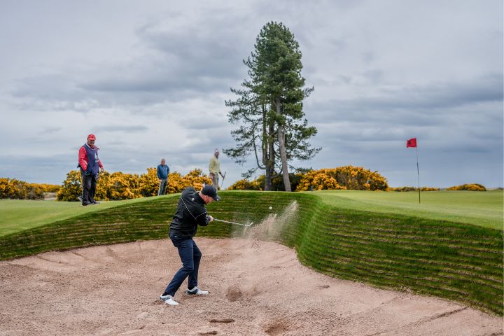 Golfer hitting a ball straight out of the bunker on the fairway in St Andrews.